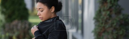 Sad multiracial woman wearing jacket on blurred urban street, banner 