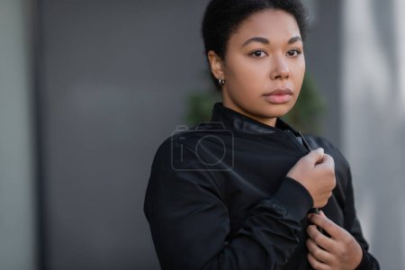 Photo for Multiracial woman with depression wearing jacket and looking at camera on urban street - Royalty Free Image