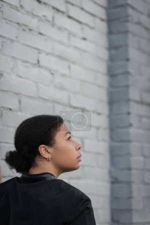 Téléchargez les photos : Vue latérale de la femme multiraciale avec problème psychologique debout près du mur de briques - en image libre de droit