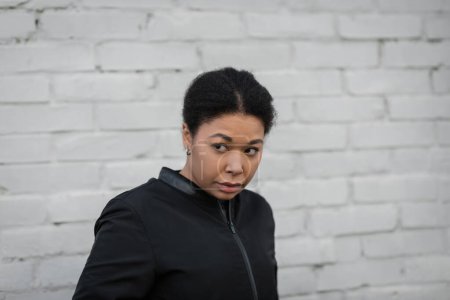 Displeased multiracial woman in jacket looking away on urban street 