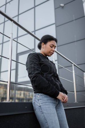 Niedriger Blickwinkel auf eine depressive Frau, die in der Nähe eines verschwommenen Gebäudes im Freien steht 