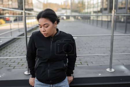 multiracial woman with mental problem standing near railing on urban street 
