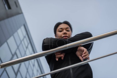 Bottom view of multiracial woman with mental problem looking at camera near railing on urban street 