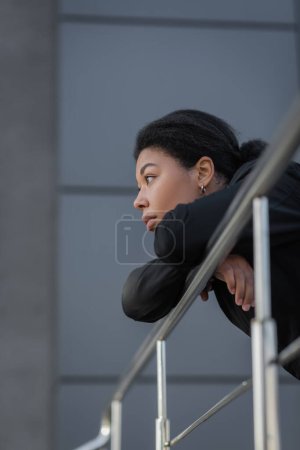 Téléchargez les photos : Jeune femme multiraciale avec apathie regardant loin près de rambarde à l'extérieur - en image libre de droit