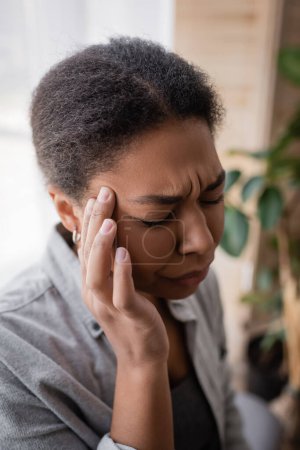 Müde multiethnische Frau leidet zu Hause unter Kopfschmerzen 