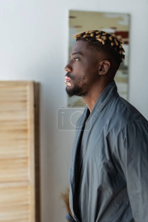 Side view of african american man with vitiligo in robe standing at home