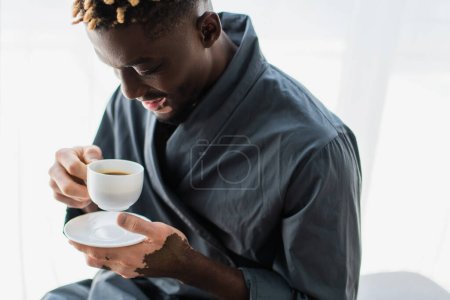 Unbekümmerter afrikanisch-amerikanischer Mann mit Vitiligo, der zu Hause eine Tasse Kaffee hält 