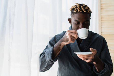 Junger afrikanisch-amerikanischer Mann mit Vitiligo trinkt morgens zu Hause Kaffee 