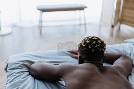 Rückenansicht des hemdslosen afrikanisch-amerikanischen Mannes mit Vitiligo auf dem Bett liegend 