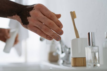 Cropped view of african american man with vitiligo taking toothbrush in bathroom 