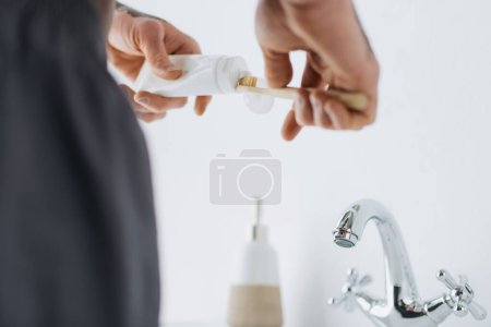 Photo for Cropped view of african american man with vitiligo squeezing toothpaste on toothbrush near sink in bathroom - Royalty Free Image