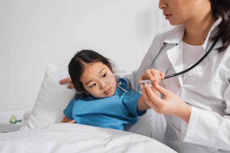 little asian child touching stethoscope near pediatrician in hospital ward