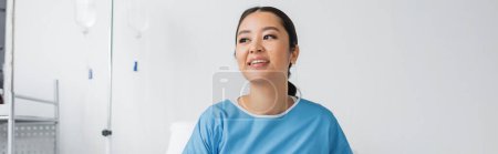 young asian woman in hospital gown smiling and looking away in clinic, banner