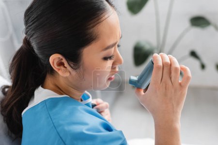 Foto de Vista lateral de la mujer asiática enferma sosteniendo inhalador en la sala de hospital - Imagen libre de derechos