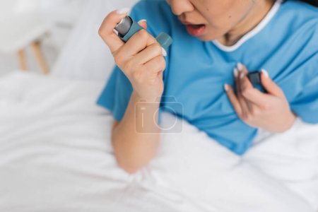 vista parcial de la mujer enferma en bata de hospital usando inhalador en la clínica