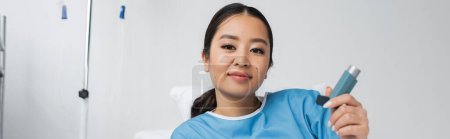 Foto de Mujer asiática complacida sosteniendo inhalador y mirando la cámara en la clínica, pancarta - Imagen libre de derechos