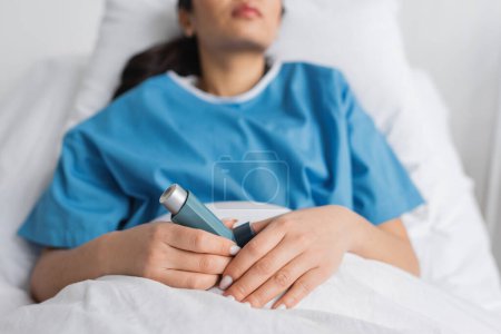 cropped view of blurred woman holding inhaler while lying on bed in clinic