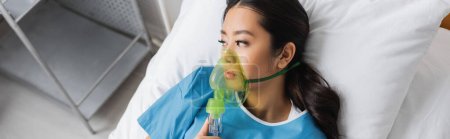 top view of depressed asian woman in oxygen mask looking away on bed in hospital ward, banner