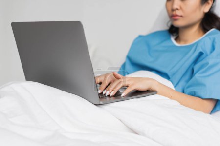 Foto de Vista parcial de la mujer asiática escribiendo en el ordenador portátil en la cama en la sala de hospital - Imagen libre de derechos