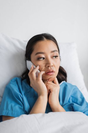 thoughtful asian woman talking on smartphone and looking away in hospital