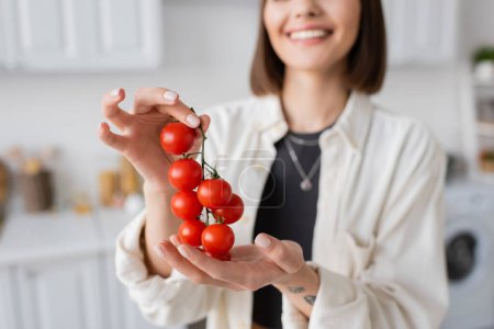 Téléchargez les photos : Vue recadrée d'une femme souriante floue tenant des tomates cerises dans la cuisine - en image libre de droit