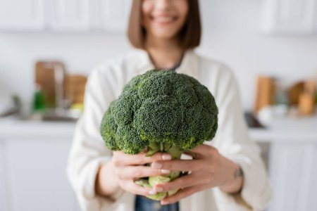 Cropped view of blurred woman holding fresh broccoli in kitchen 