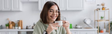 Fröhliche junge Frau mit Brille und Kaffee in verschwommener Küche, Transparent 
