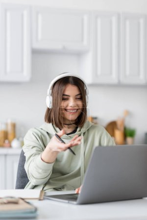Freelance positif dans les écouteurs ayant appel vidéo sur ordinateur portable flou à la maison 