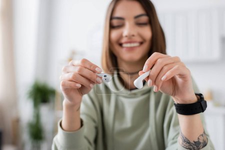 Smiling tattooed woman holding wireless earphones at home 