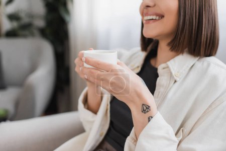 Ausgeschnittene Ansicht einer unbeschwerten tätowierten Frau mit einer Tasse Kaffee im Wohnzimmer 