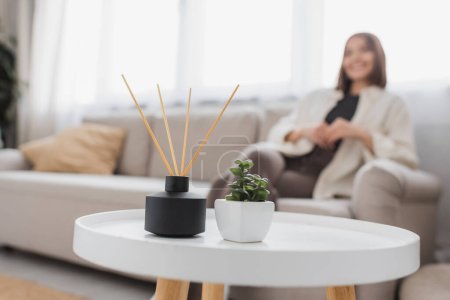 Bambus-Duftstäbchen und Pflanze auf Couchtisch neben verschwommener Frau zu Hause 