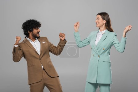 Photo for Excited interracial event hosts in formal wear showing yes gesture and looking at each other during holiday while standing isolated on grey - Royalty Free Image