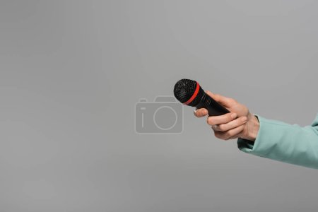 Foto de Vista recortada de la mano del anfitrión del evento en chaqueta azul que sostiene el micrófono negro e inalámbrico durante las vacaciones mientras está de pie aislado en gris - Imagen libre de derechos