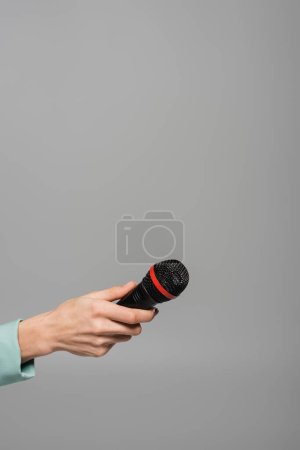 Ausgeschnittene Ansicht eines schwarzen drahtlosen Mikrofons in der Hand des Veranstalters in grüner Jacke während eines Auftritts im Urlaub, während er isoliert auf grau steht  