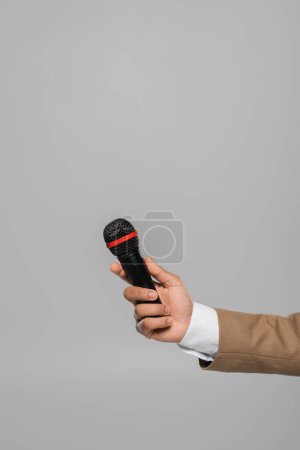 Cropped view of young event host in blue jacket and white shirt holding wireless microphone while standing isolated on grey with copy space 