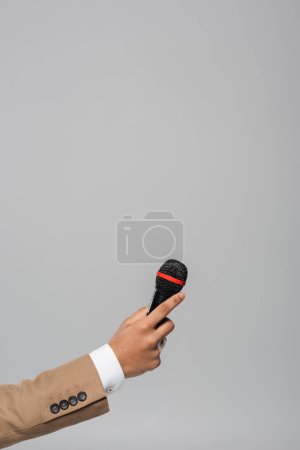 Widok na rękę gospodarza imprezy w brązowej kurtce z bezprzewodowym mikrofonem podczas występu odizolowany na szaro z przestrzenią do kopiowania 