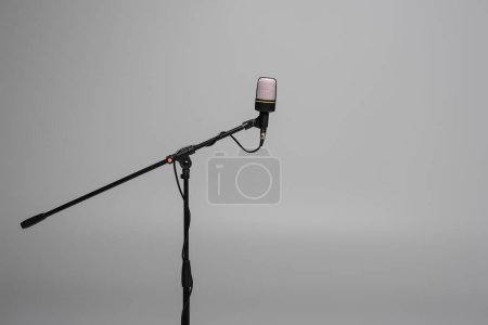 Black microphone with wire on metal stand isolated on grey with copy space, studio shot 