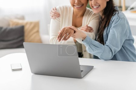 recortado vista de alegre interracial lgbt pareja mostrando anillo de compromiso durante la videollamada 