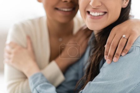 cropped view of multiracial lesbian woman with engagement ring hugging girlfriend 