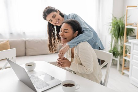 joyful multiethnic lesbian couple showing engagement ring during video call at home 