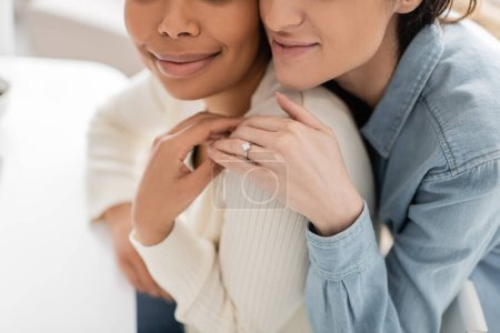 partial view of engaged multiracial lesbian women with engagement ring hugging each other 