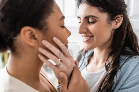 Verlobte lesbische Frau mit Ehering lächelt und umarmt multirassischen Partner 