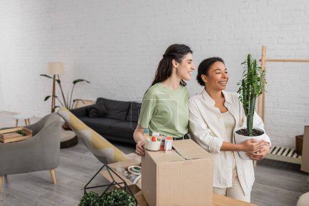 cheerful interracial lgbt couple smiling while moving into new house 