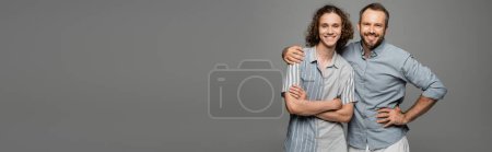 happy father hugging shoulder of positive teenage son isolated on grey, banner 