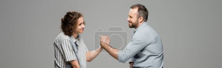 Téléchargez les photos : Vue latérale du père heureux et du fils adolescent serrant la main isolés sur gris, bannière - en image libre de droit