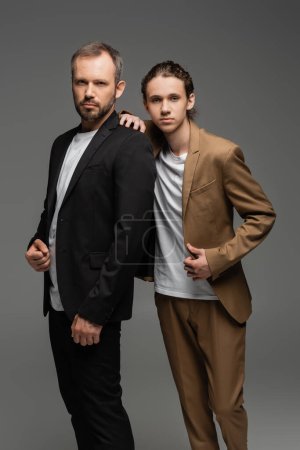 well dressed dad and teenage son in suits standing together isolated on grey 
