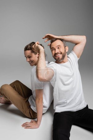 cheerful father having fun with teenage son in white t-shirt and sitting on grey 