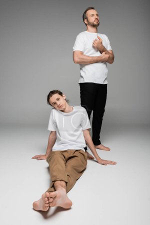 full length of father standing next to teenage son in white t-shirt on grey 