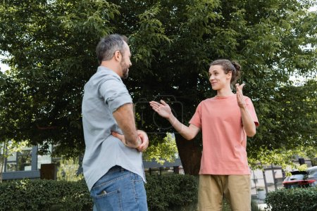 happy teenage boy showing big gesture with hands near bearded father in park 