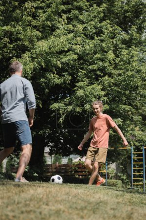 Foto de Alegre adolescente jugando al fútbol con su padre en verde parque de verano - Imagen libre de derechos